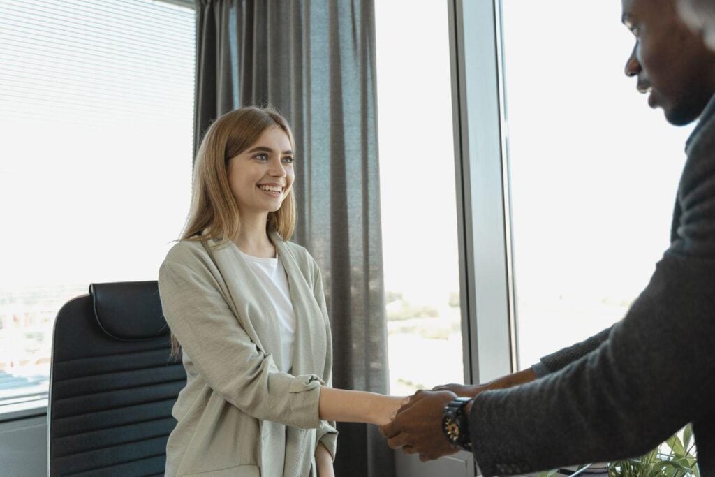 Smiling female candidate shaking hands with a hiring manager in an office after accepting a job offer