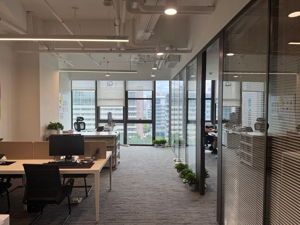 Quiet open-plan office with empty desks, plants and glass-walled rooms with blinds, designed to protect focus time