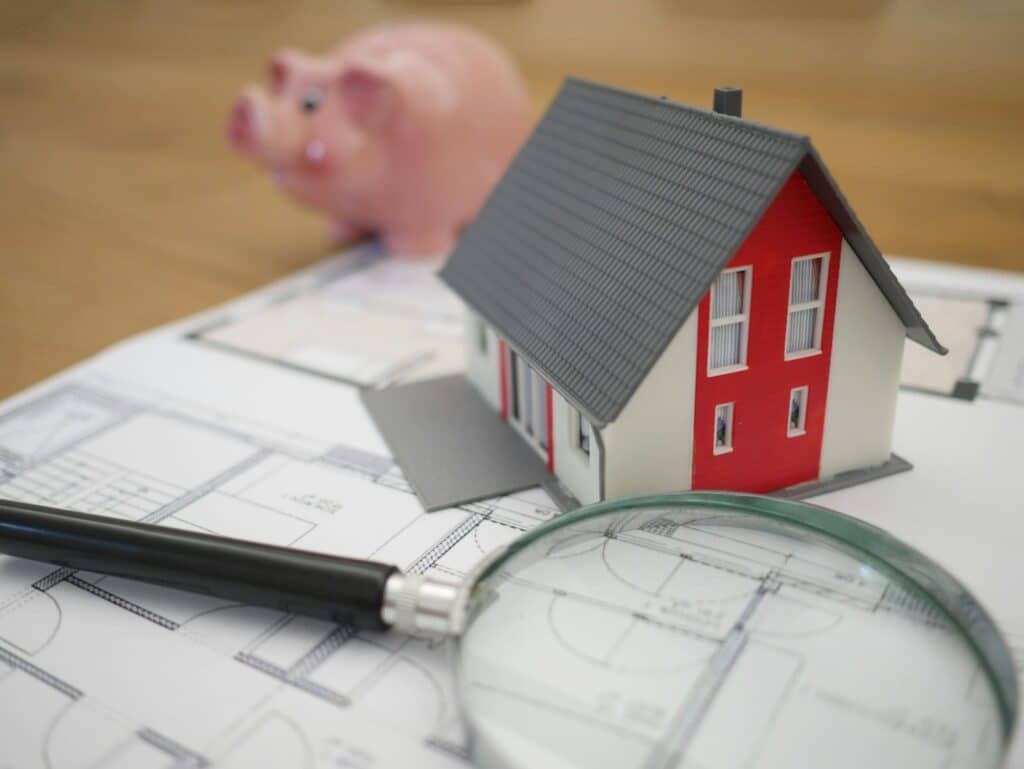 Magnifying glass over house floor plans beside a model home, representing a home inspection